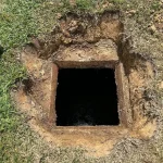 Close up of a dark septic hole tank surrounded by grass.