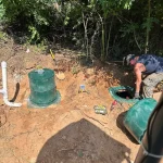A septic tank expert hovers above a septic tank entry hole. He looks down at it.