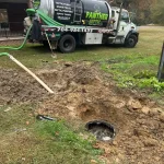 A septic tank vacuum truck parked on a residential backyard. A drainage pipe extends close to a septic tank entry hole in the ground.
